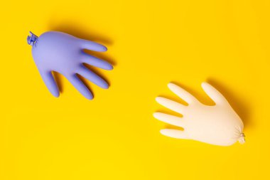 Stüdyoda parlak sarı bir arka planda beyaz ve mor lateks eldivenler. Üst görünüm yatay fotoğraf.