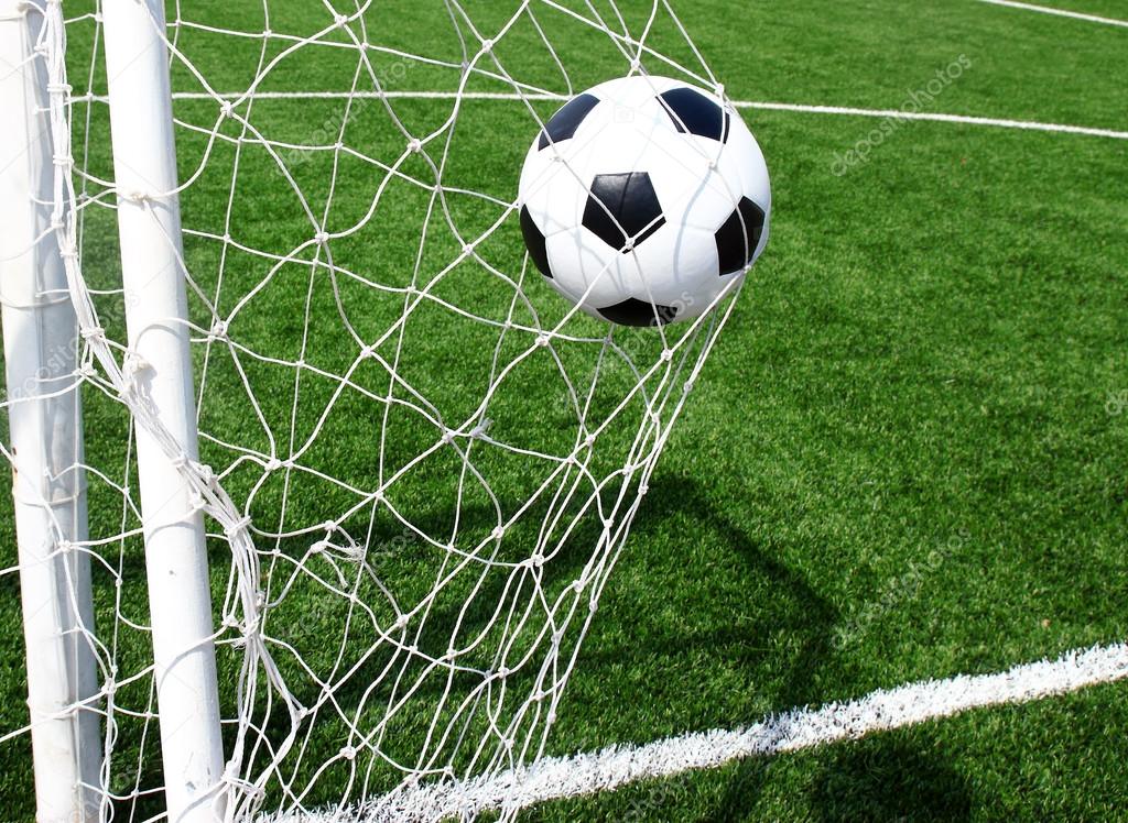 Soccer football in Goal net with green grass field