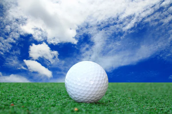 Golf topu mavi gökyüzü ve beyaz bulutlar karşı çimenlerin üzerinde — Stok fotoğraf