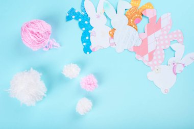 Paskalya tavşanı dekorasyon kağıdı arka planda kesilmiş. Renkli tavşanlardan ve el sanatları aletlerinden oluşan bir Noel tatili çelengi. Mavi arkaplanda kopyalama alanı olan üst görünüm