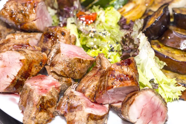 Viande rôtie sur un gril avec des légumes sur une assiette en bois — Photo