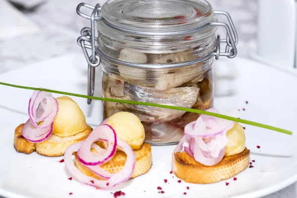 Ingelegde haringen in een glazen pot met aardappel canapeetjes — Stockfoto