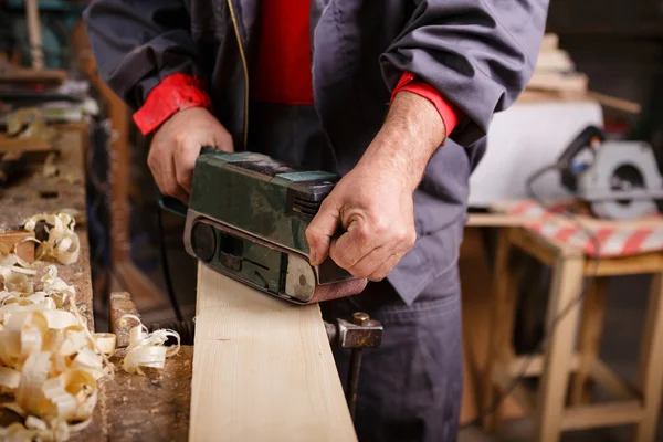 Joiner with a belt sander on a wooden board — Stock Photo, Image