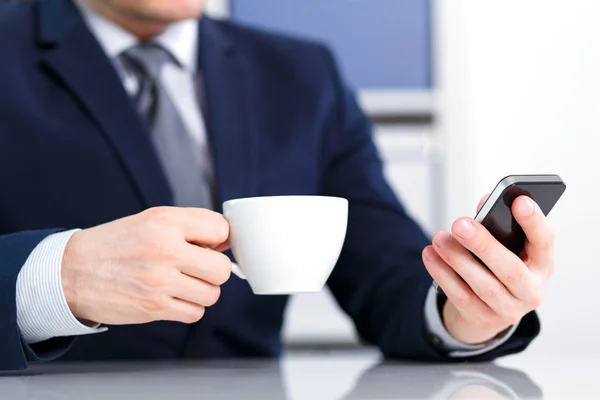 Homme d'affaires tenant un téléphone portable et un café — Photo