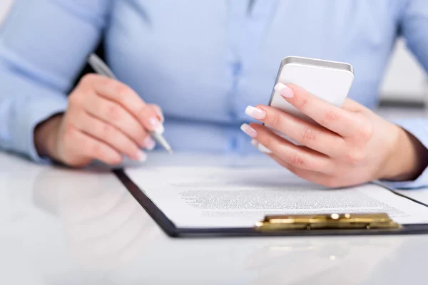 Молодая женщина работает с мобильным телефоном и держит ручку — стоковое фото