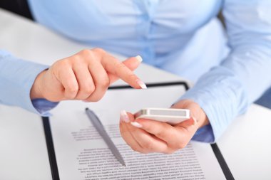Sözleşme üzerinde bir cep telefonu ile çalışan genç kadın