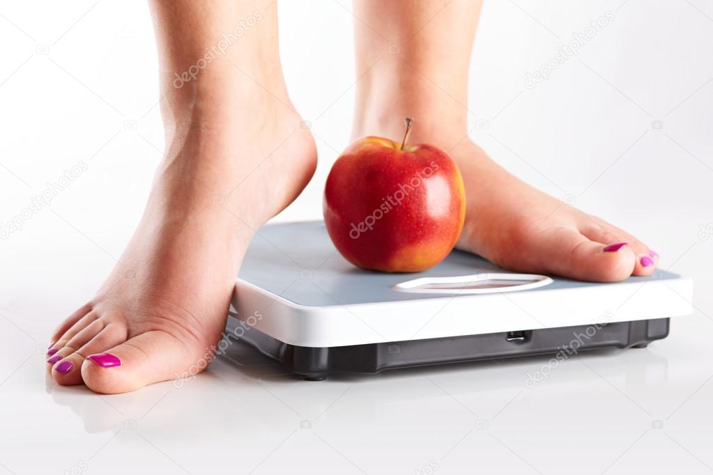 A pair of female feet standing on a bathroom scale with red appl