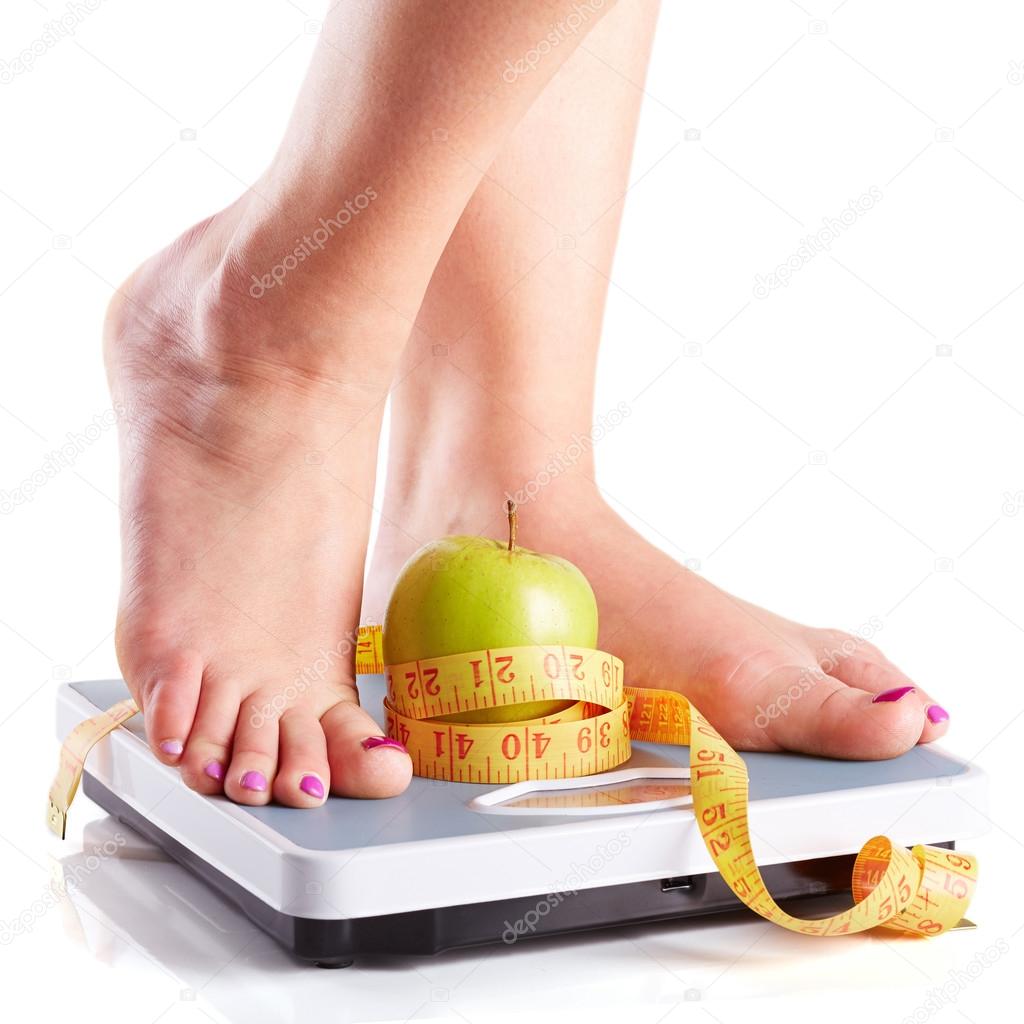 A pair of female feet standing on a bathroom scale with green ap