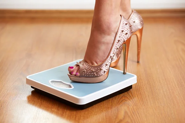 Female feet in golden stilettos on a weight scale — Stock Photo, Image