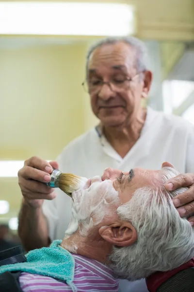 Homem sênior no trabalho como barbeiro barbeando cliente — Fotografia de Stock