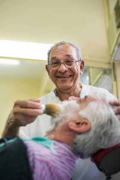 Uomo anziano al lavoro come barbiere rasatura cliente — Foto Stock