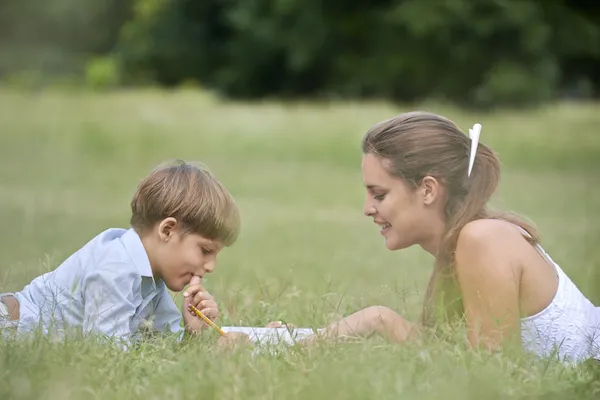 Mamma aiutare il figlio con i compiti, sdraiati sull'erba — Foto Stock