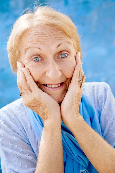 Portrait of surprised senior woman with hands on face on blue ba — Stock Photo, Image