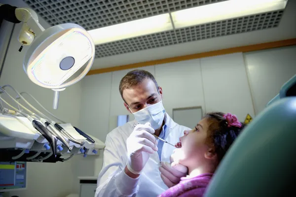 Tandarts controleren tanden van jonge meisje liggend op Bank — Stockfoto