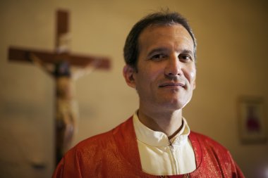 Portrait of happy catholic priest smiling at camera in church clipart