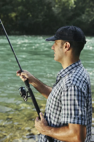 Pescador de pé perto do rio e segurando vara de pesca — Fotografia de Stock