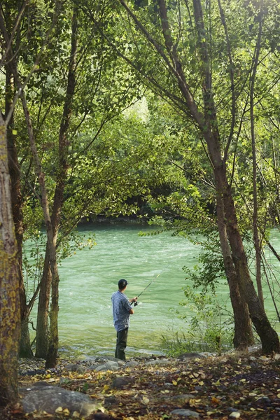 Pescador de pie cerca del río y sosteniendo caña de pescar —  Fotos de Stock