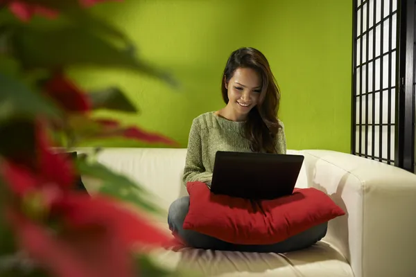 Asian girl with computer sitting on sofa at home — Stock Photo, Image