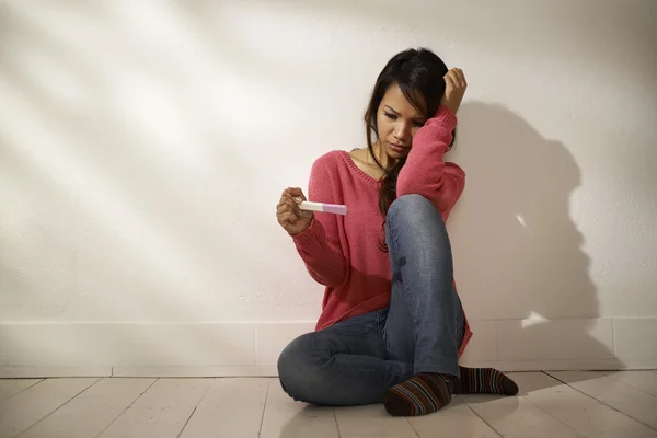 Triste menina asiática olhando para teste de gravidez sentado no chão — Fotografia de Stock