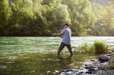 Fisherman standing near river and holding fishing rod clipart