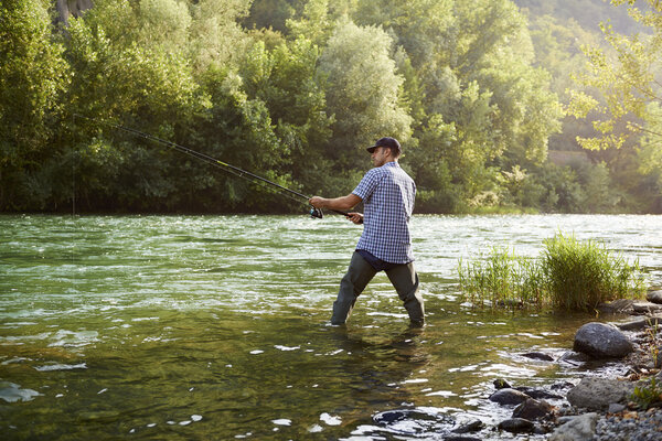 Fisherman standing near river and holding fishing rod