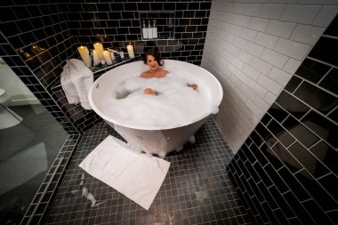 Muhteşem bir esmer model, yuvarlak bir küvette banyo yaparken çıplak poz verir.