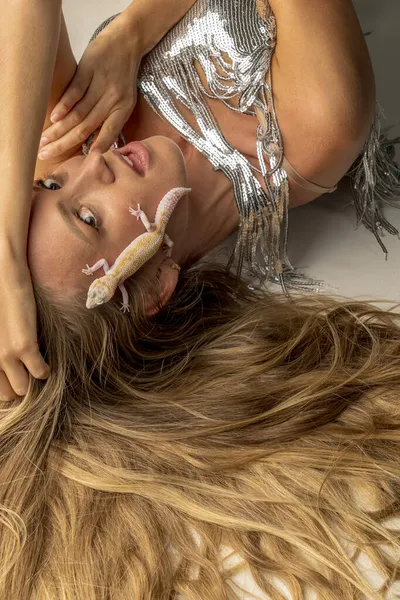 Sarışın bir model stüdyo ortamında bir kertenkeleyle poz veriyor.