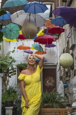 Çok sayıda renkli şemsiyenin altında muhteşem bir sarışın model poz veriyor.