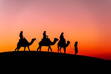 Three passengers and their handler travel in the Saharan Desert in Morocco clipart