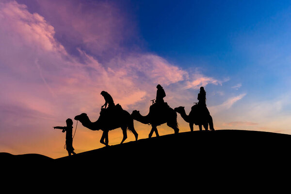Three passengers and their handler travel in the Saharan Desert in Morocco
