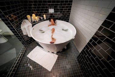 Muhteşem bir esmer model, yuvarlak bir küvette banyo yaparken çıplak poz verir.