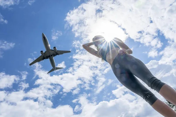 美しいブロンドモデルは夏の日を楽しんでいますが 民間航空機は頭上を飛ぶ — ストック写真