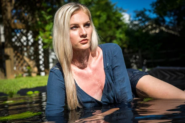 Sarışın bir manken, iç çamaşırlarıyla su havuzunda poz veriyor.