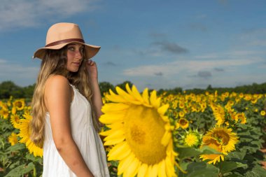 Sarışın bir model, ayçiçeği tarlasında poz veriyor.