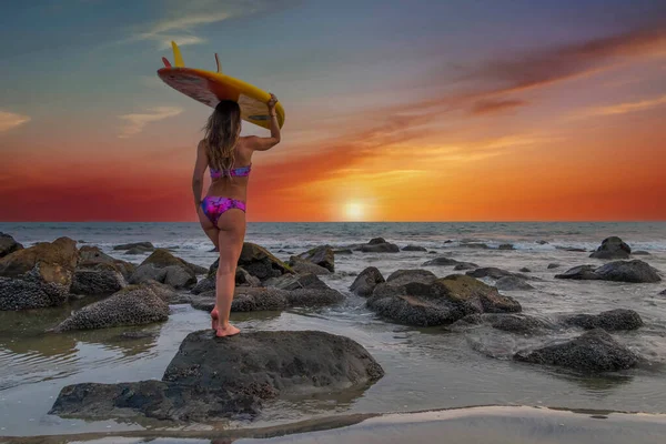 Gün batımında sörf tahtasıyla sahilde poz veren güzel esmer bir İspanyol manken.