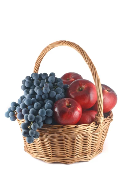 Cesta de mimbre con manzanas rojas y uvas azules — Foto de Stock