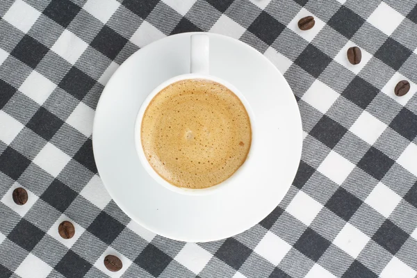 Grãos de café e xícara de café em uma toalha de mesa quadriculada — Fotografia de Stock