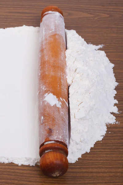 Rolling out dough with a rolling pin on a brown wooden table — Stock Photo, Image
