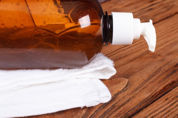 Liquid soap dispenser and a white towel on the oak table — Stock Photo, Image