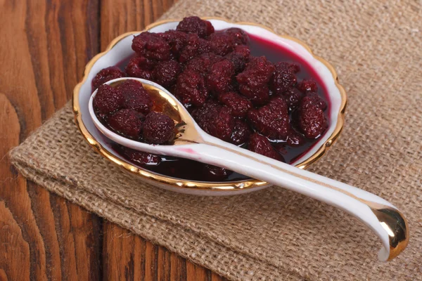 Raspberry jam in a saucer with a spoon on a wooden table — Stock Photo, Image