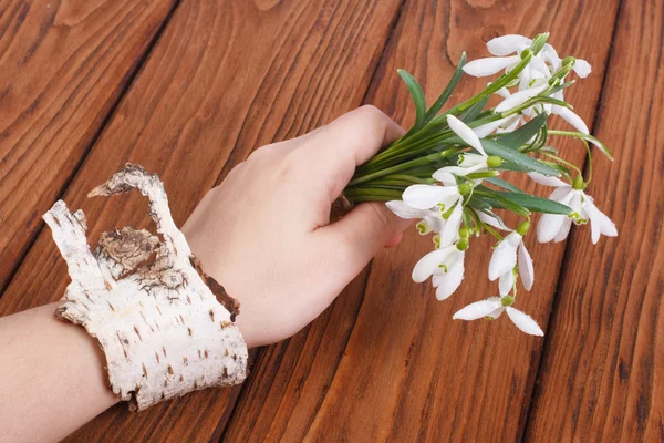 Schneeglöckchen in weiblicher Hand mit einem Armband an einer Birke — Stockfoto