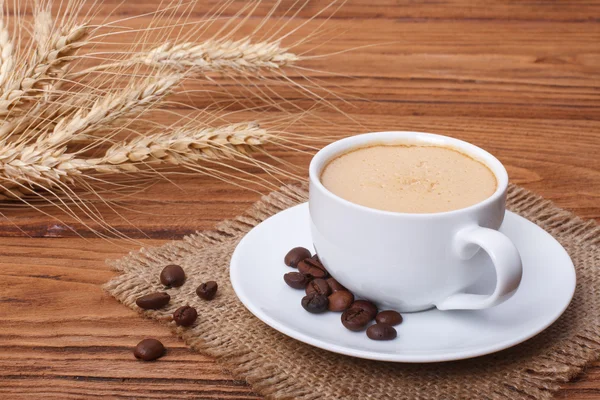 Coffee with foam and ears of wheat on the wooden table — Stock Photo, Image