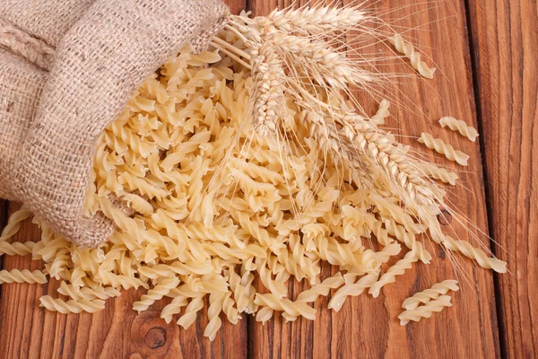 Pasta cruda y espigas de trigo derramadas de la bolsa —  Fotos de Stock