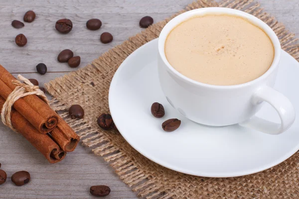 Caffè con cannella su un tovagliolo su uno sfondo di iuta di legno — Foto Stock