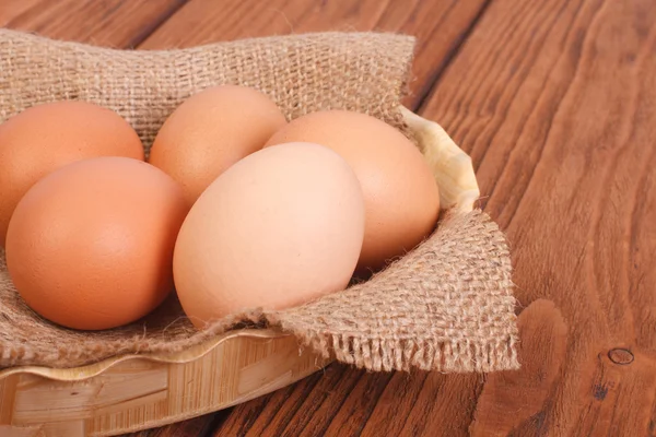 Fresh brown chicken eggs in a basket on a sacking on an oak wood table — Stock Photo, Image