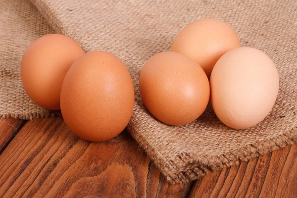 Fresh brown chicken eggs on burlap on a wooden table — Stock Photo, Image