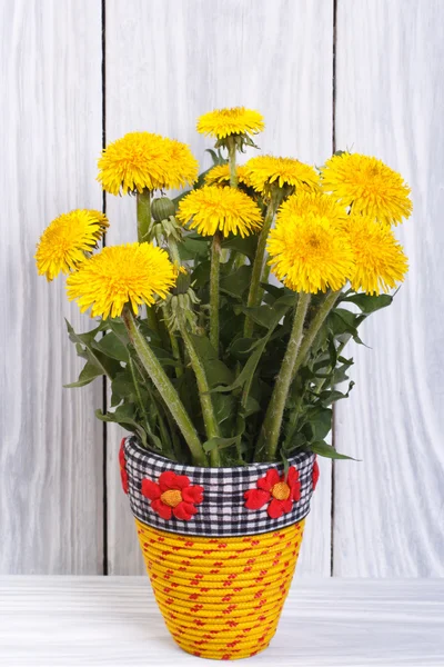 Flores de diente de león en un jarrón amarillo sobre un fondo de tablas de madera — Foto de Stock