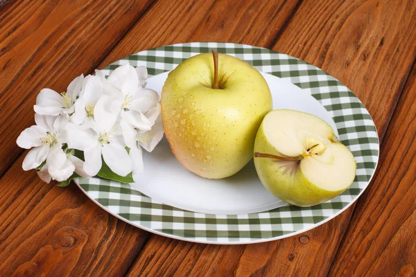 Green apple on a white plate and flowers on a brown wooden table — Stock Photo, Image