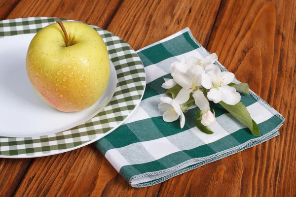 Whole green apple with flowers on a white plate on a table — Stock Photo, Image