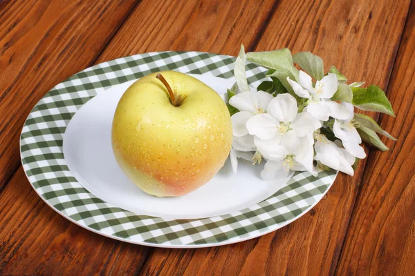 Whole green apple with flowers on a white plate on a table — Stock Photo, Image